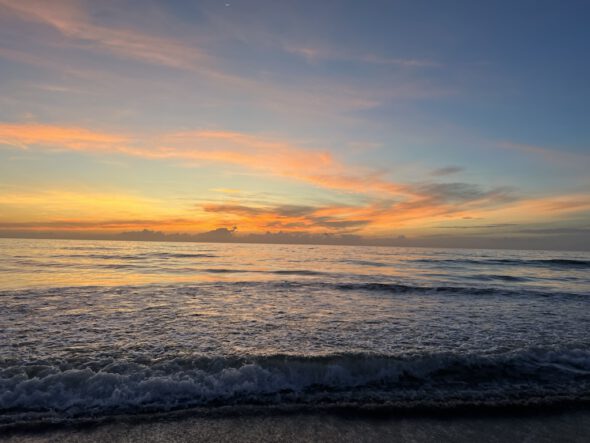 A sunset over the ocean with waves in the background.