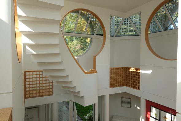 Modern interior with floating staircase, circular windows, and geometric design elements featuring lattice accents and daylight streaming in.